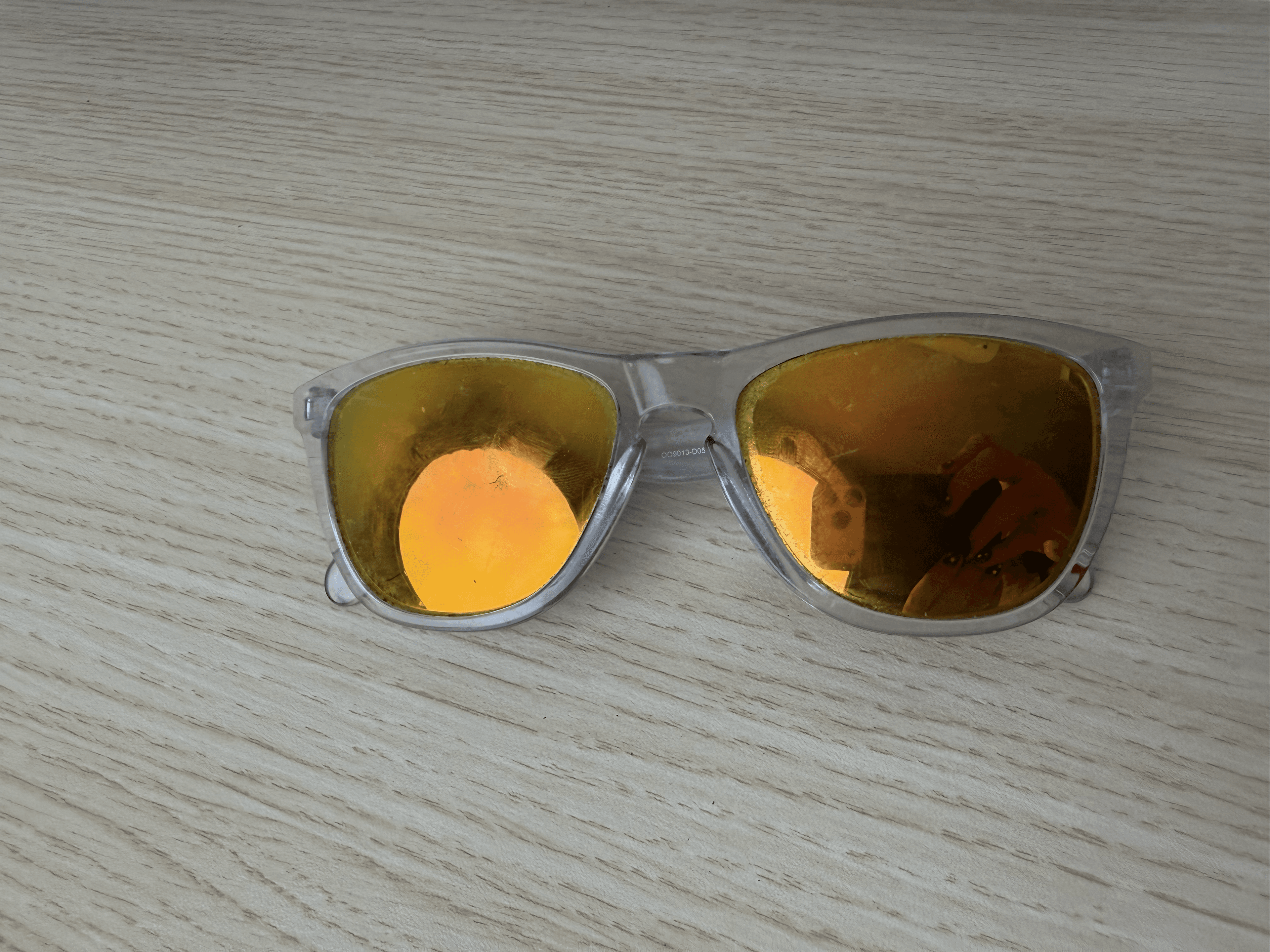 Chris’s translucent Oakley Frogskins with gold mirrored lenses resting on a pale wooden surface.