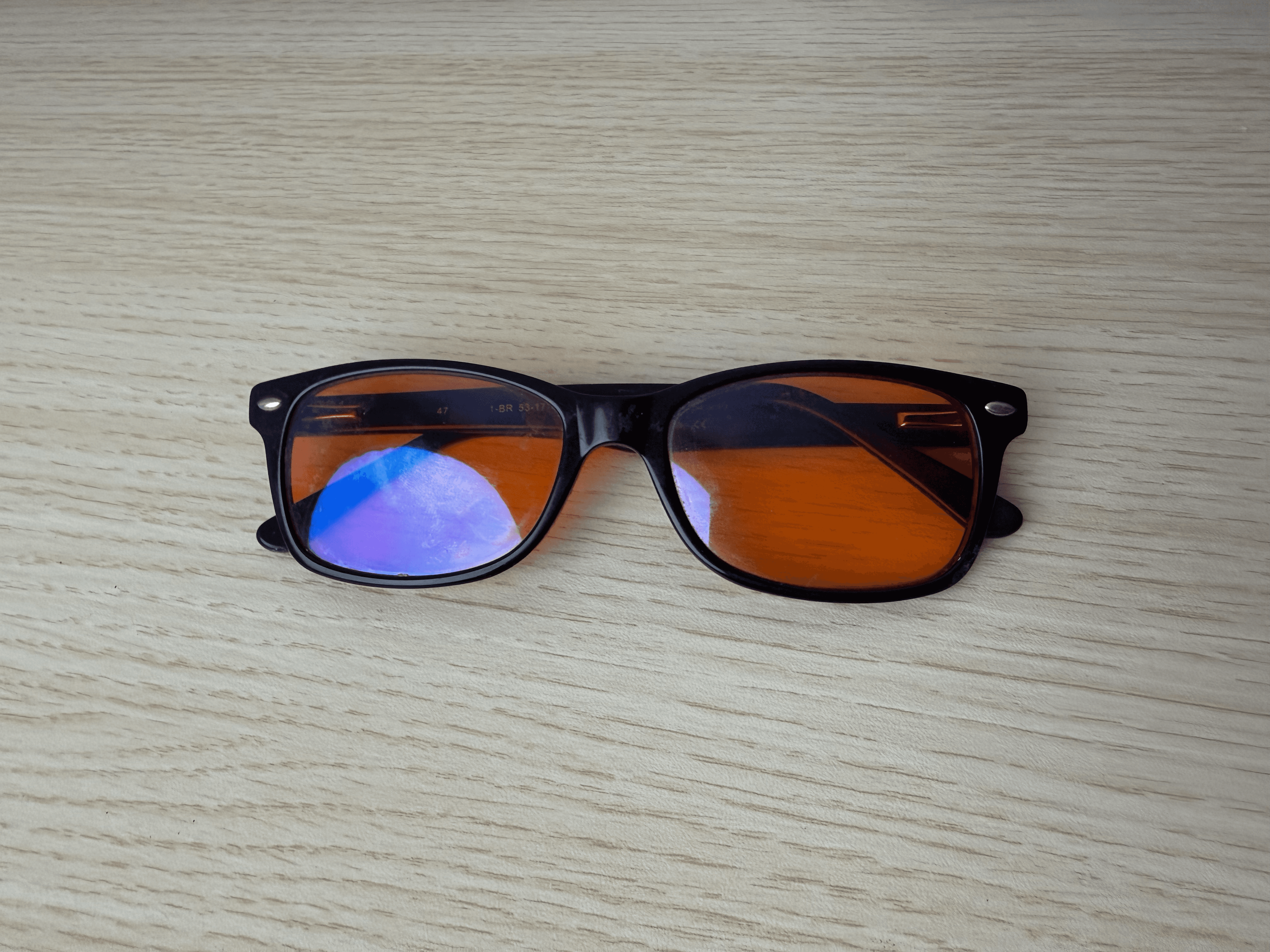 Chris’s black Swanwick frames with amber lenses resting on a pale wooden surface.
