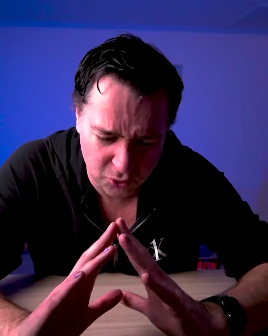 Chris Hay seated at his desk in the studio, hands together, in blue light.